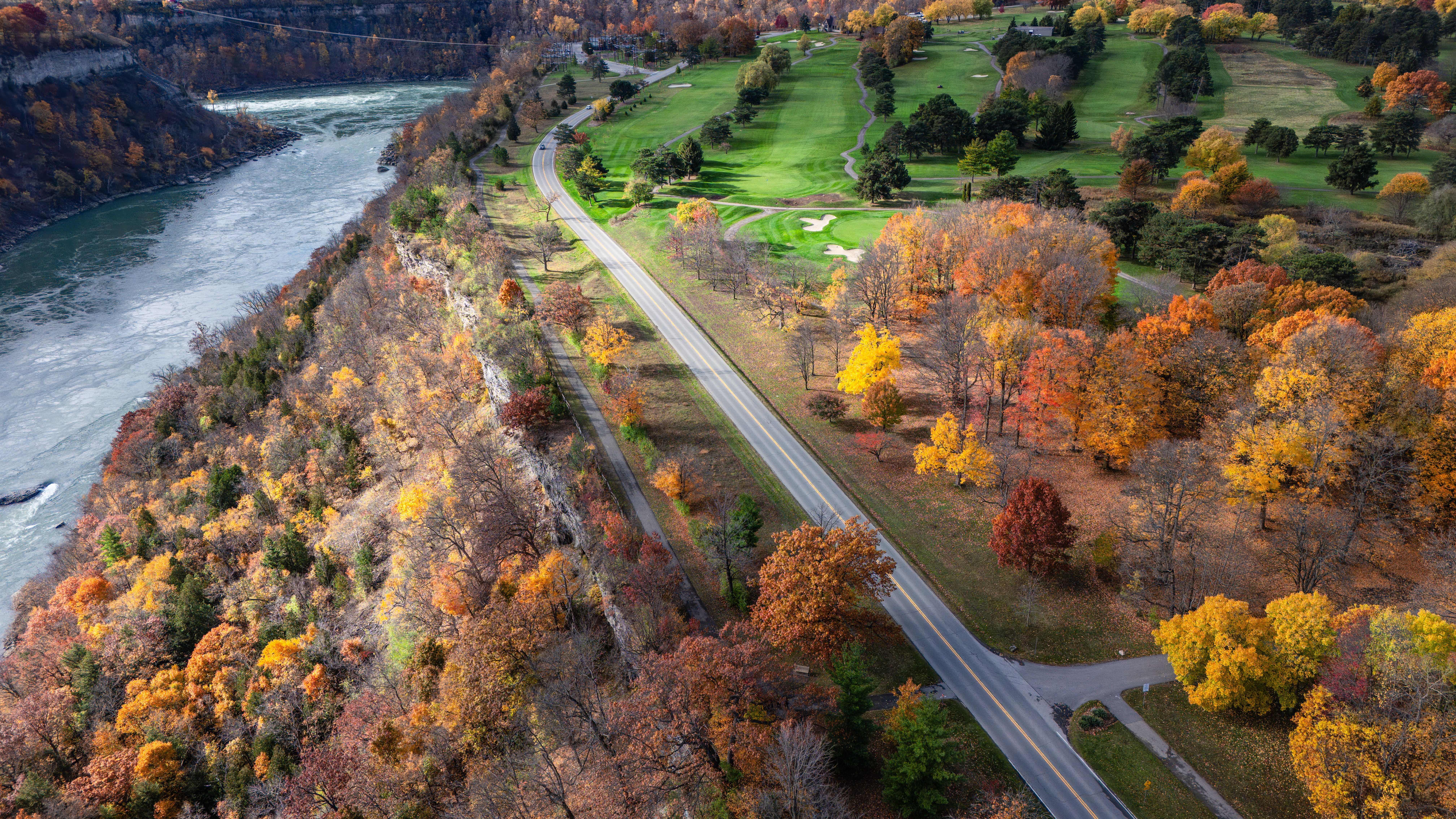 Aerial view of a vibrant fall landscape featuring a winding road, river, and golf course.
