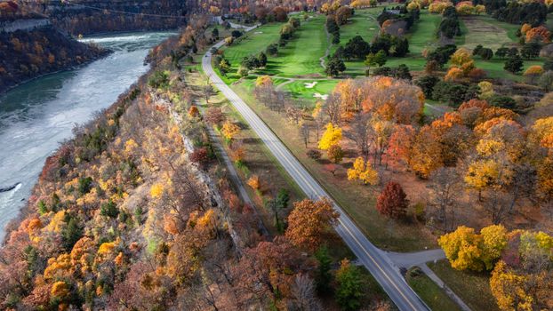 Aerial view of a vibrant fall landscape featuring a winding road, river, and golf course.