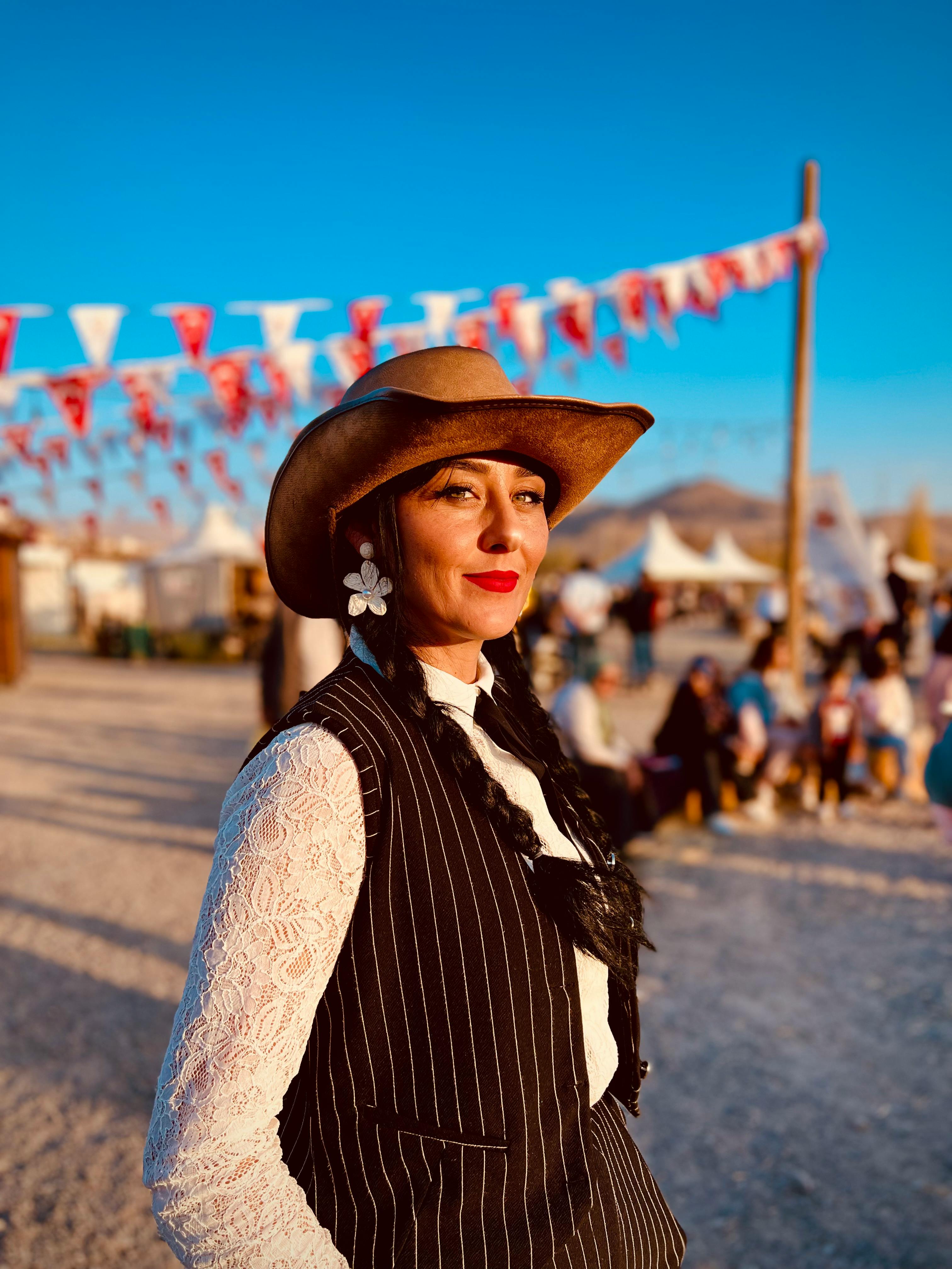 Woman in cowboy hat at an outdoor festival during sunset, lively atmosphere.