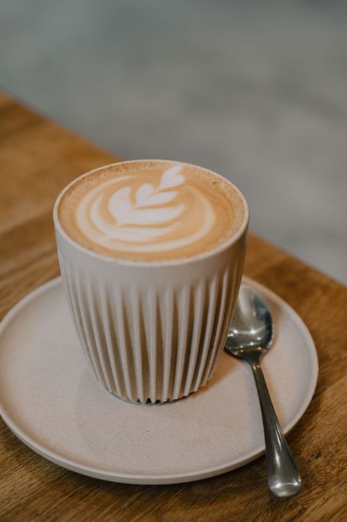 Free Cozy latte with leaf pattern in ribbed mug on rustic wooden table, perfect for a cafe setting. Stock Photo