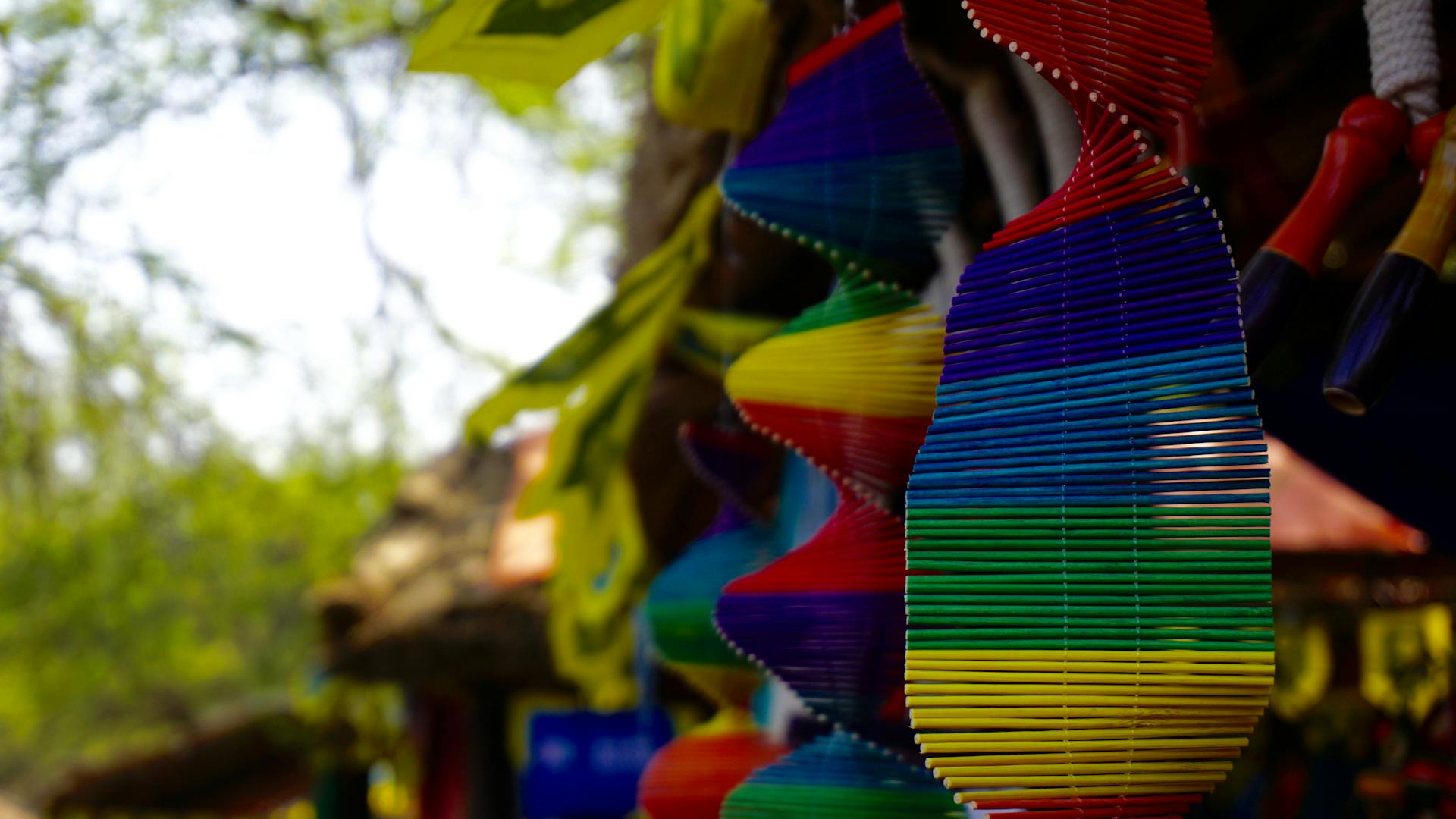 Vibrant rainbow wind chimes hanging in a lush green garden outdoors, adding decorative charm.