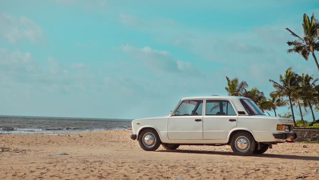 A classic white car parked on a sandy beach with palm trees and the ocean in the background, perfect for travel themes.