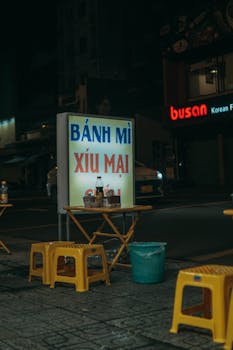 Nighttime street food setting featuring a Vietnamese bánh mì stall with seating.