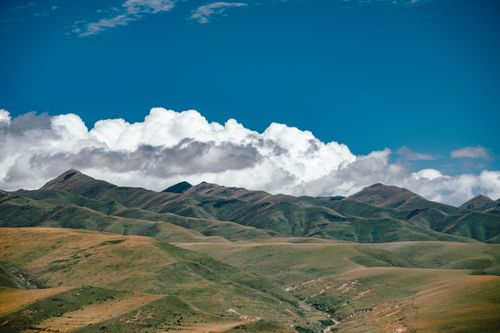Free Expansive mountain range with lush green hills and fluffy clouds beneath a vibrant blue sky. Stock Photo