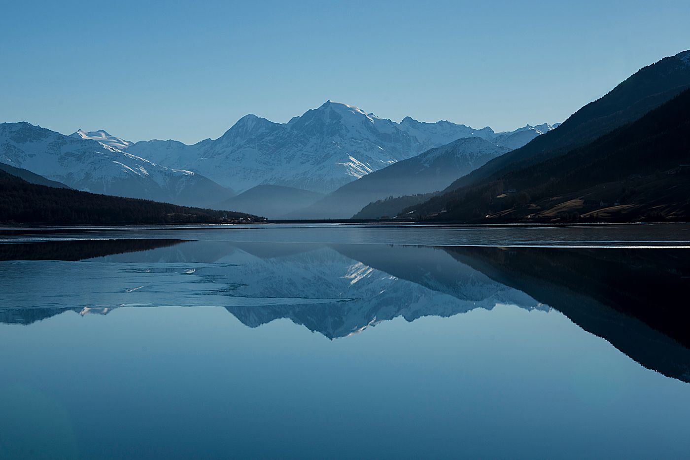 Still lake at dawn with forested mountains and soft morning light