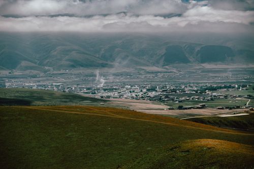 Free Scenic aerial shot of a small town nestled in a lush mountainous valley, under a cloudy sky. Stock Photo