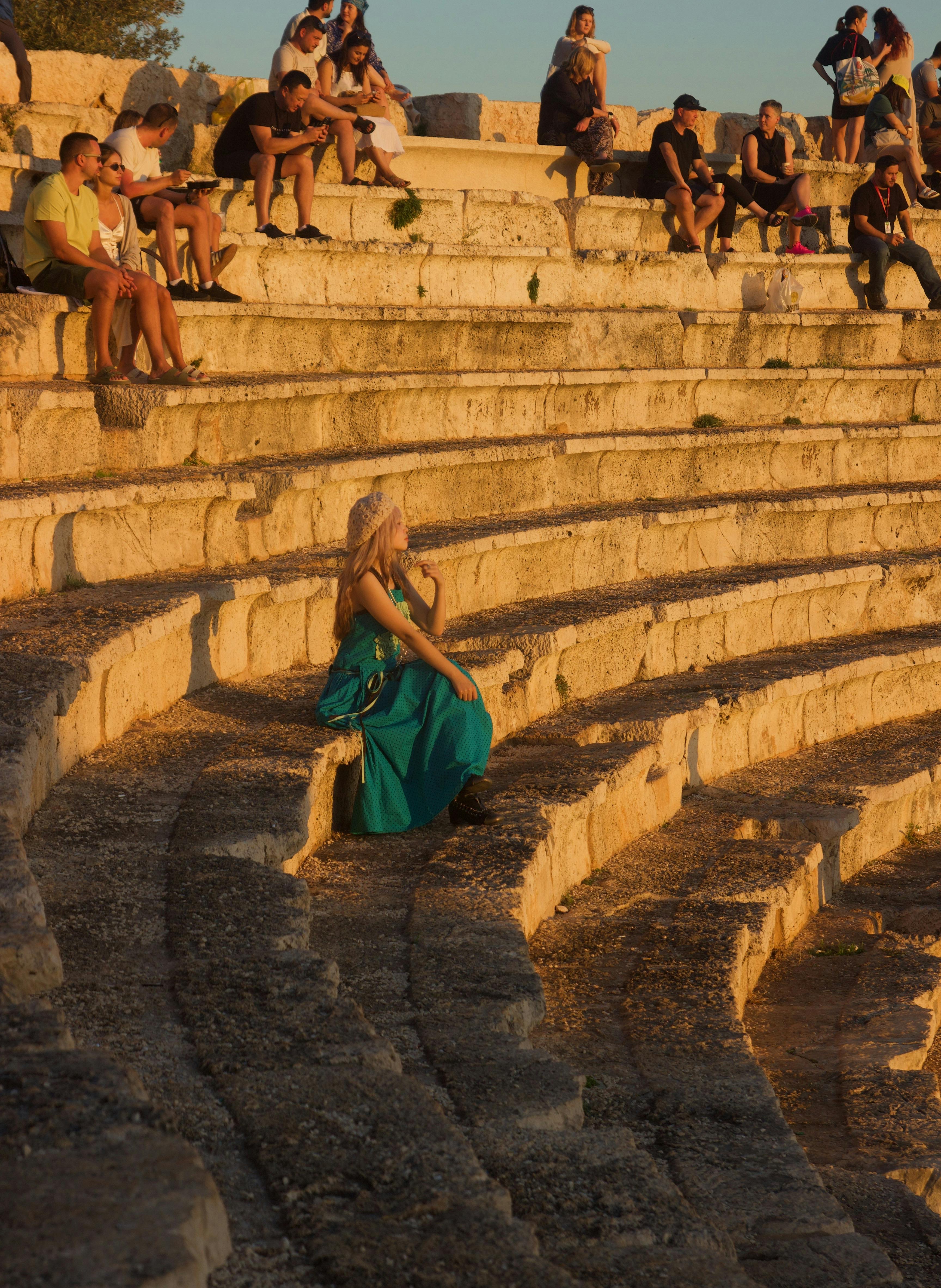 Ücretsiz Gün batımında antik amfitiyatroda oturan turkuaz elbiseli kadın. Stok Fotoğraflar