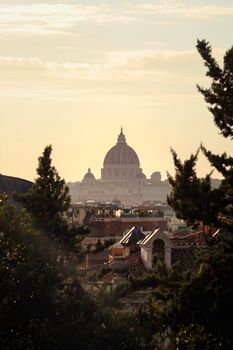 Scenic view of St. Peter's Basilica at sunset surrounded by rooftops and greenery in Rome, Italy.