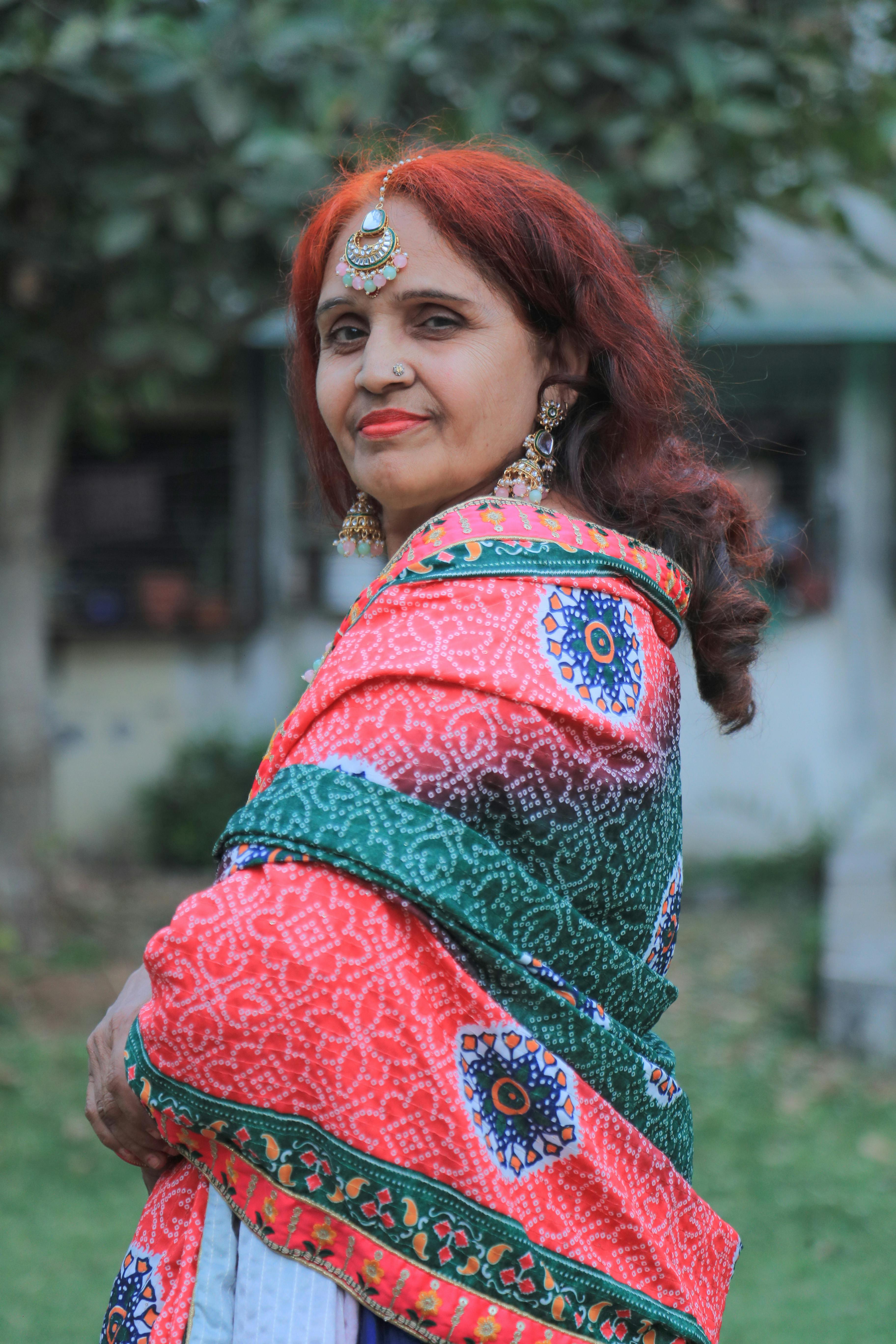 A woman posing outdoors in vibrant traditional Indian attire with intricate jewelry.