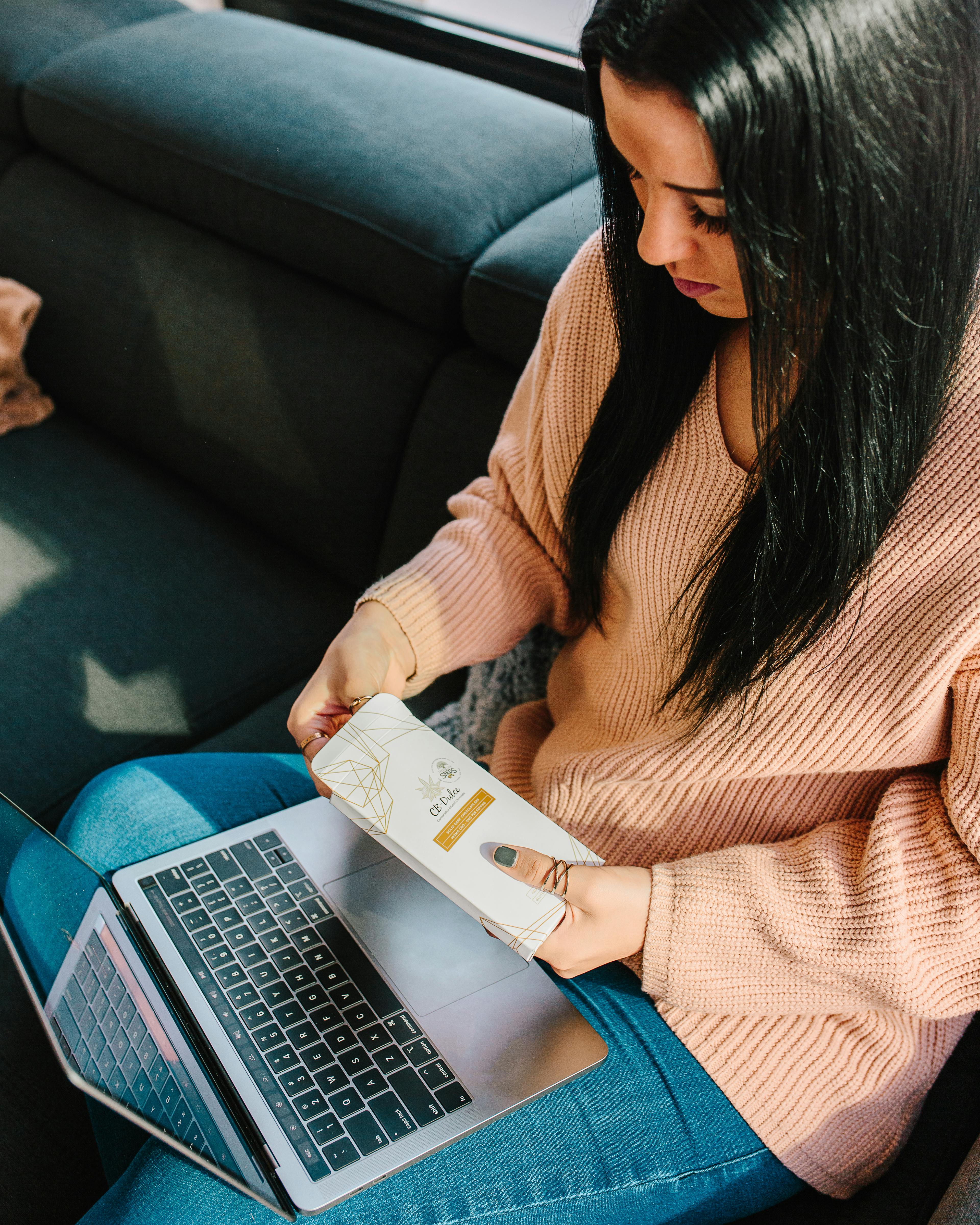 一名妇女坐在舒适的房间里，拿着书，用着笔记本电脑