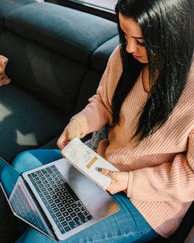 一名妇女坐在舒适的房间里，拿着书，用着笔记本电脑