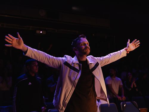 Free A man opens his arms in worship inside a dimly lit venue, expressing devotion and freedom. Stock Photo