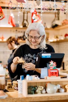 Elderly woman in a café prepping a drink during holiday season. Cozy and festive.