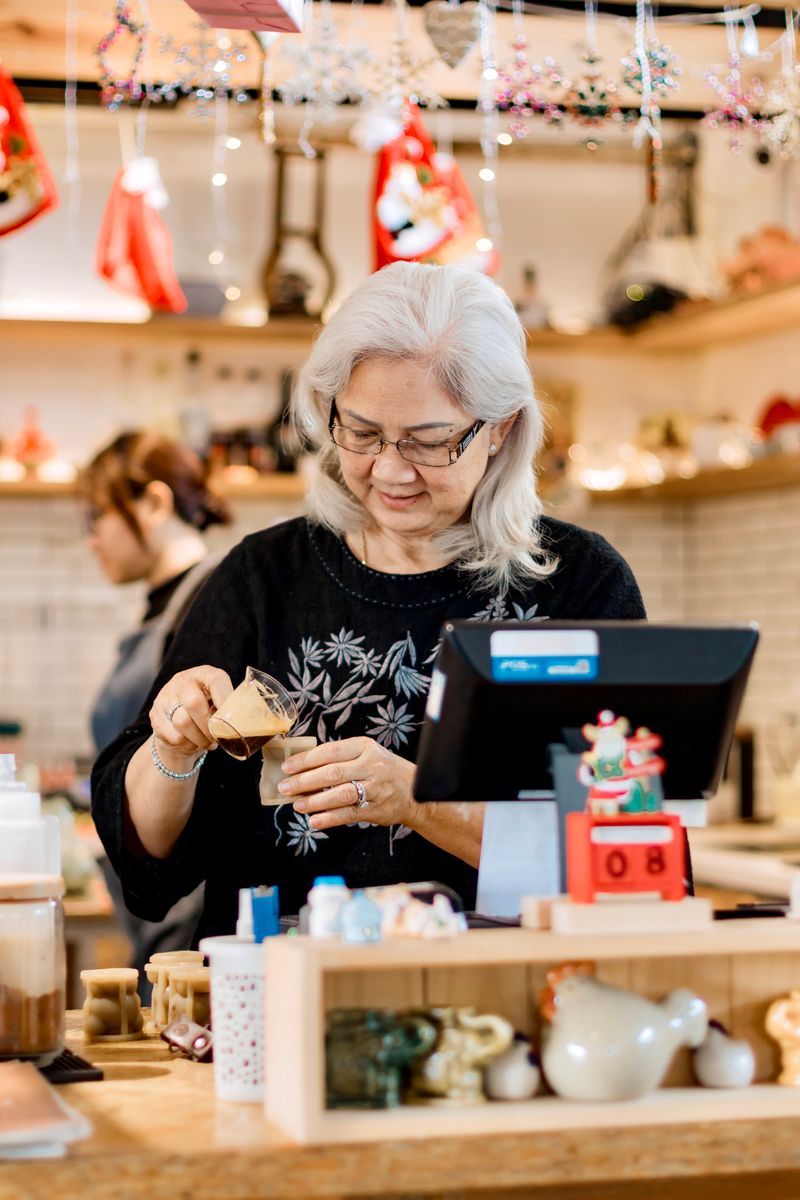 An older woman preparing a drink behind the counter of a small cafe