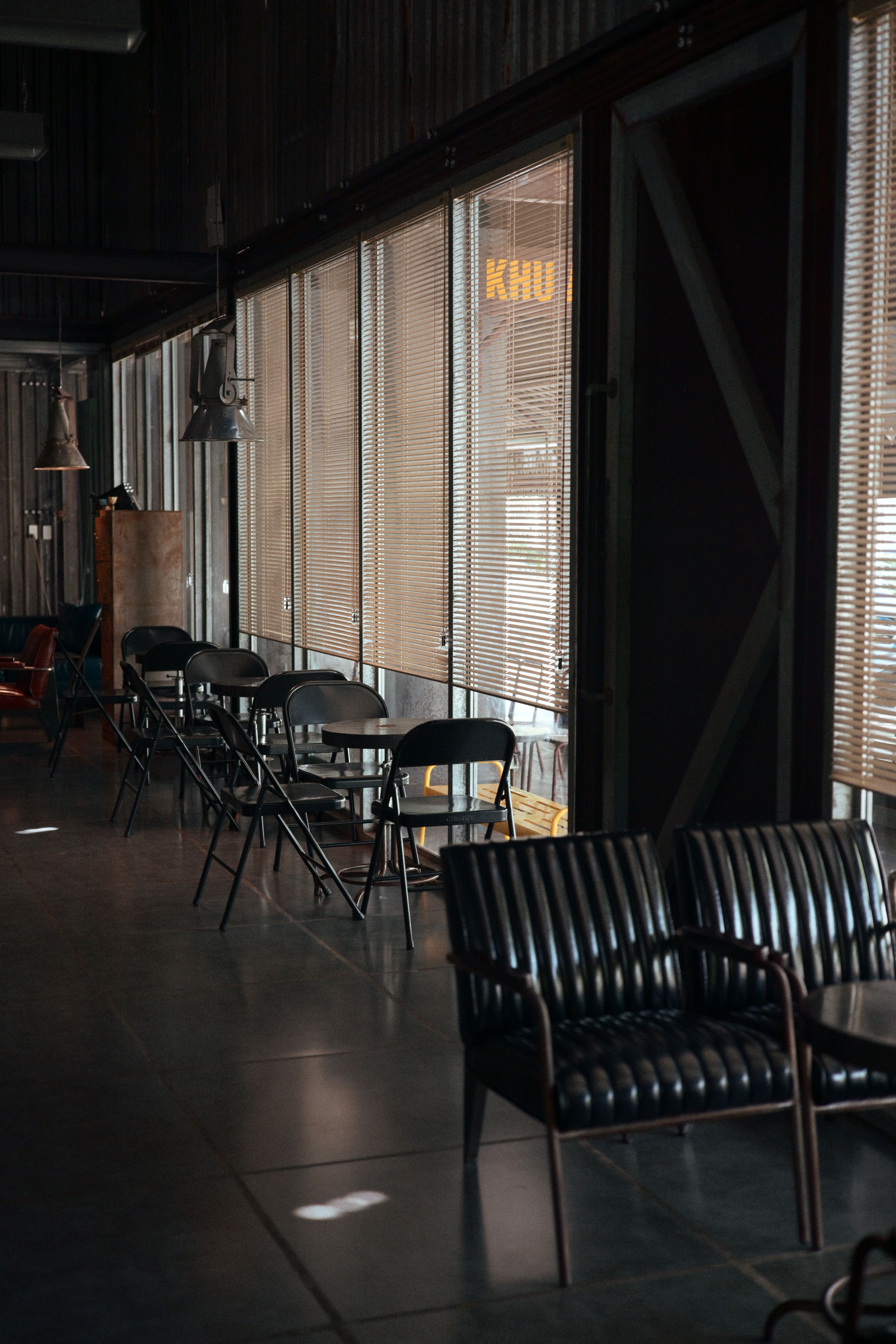 Quiet industrial-style café with empty black chairs and tables by the window, soft natural lighting.