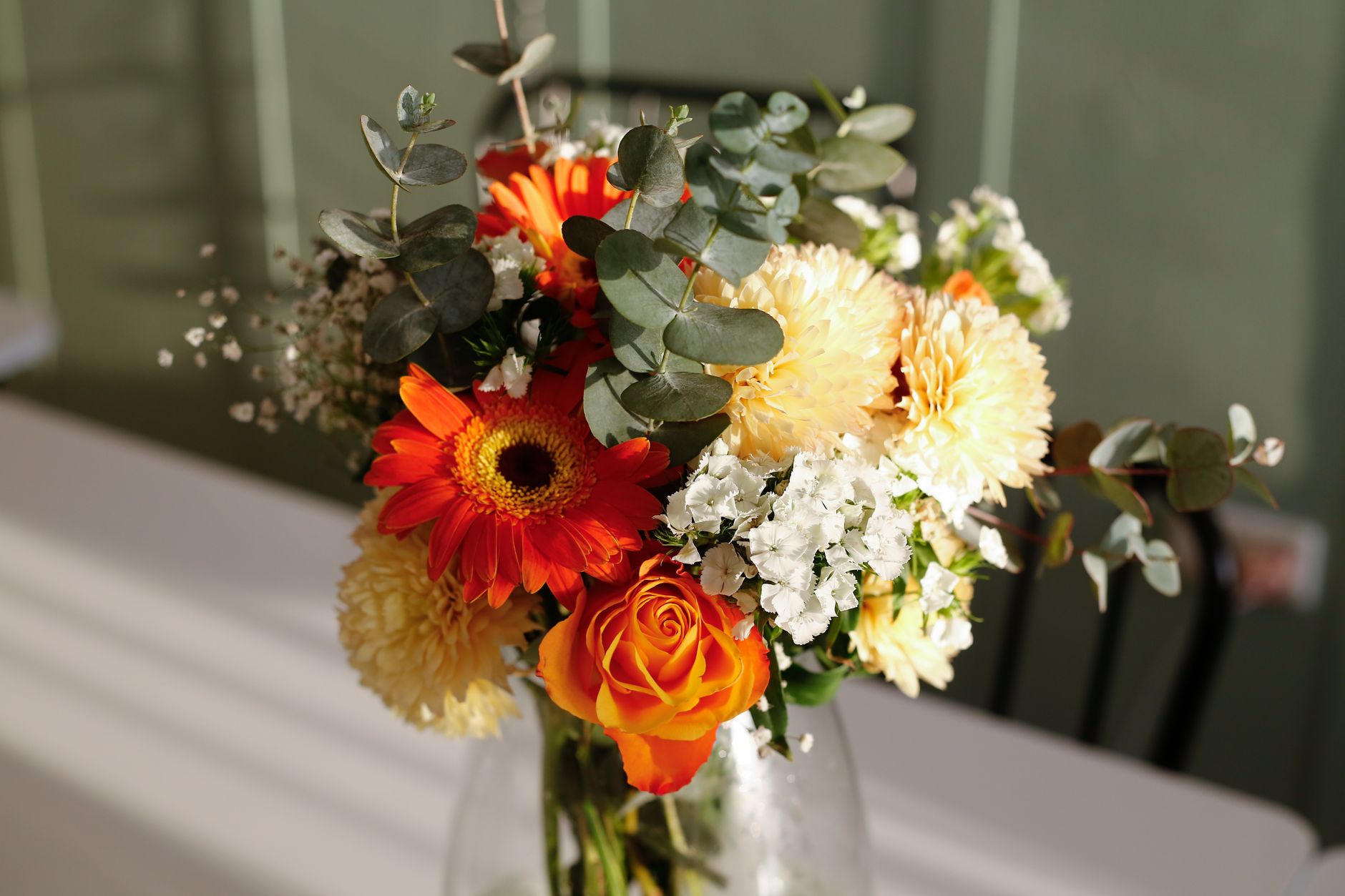 Colorful floral arrangement with gerbera daisies, roses, and eucalyptus in a vase.