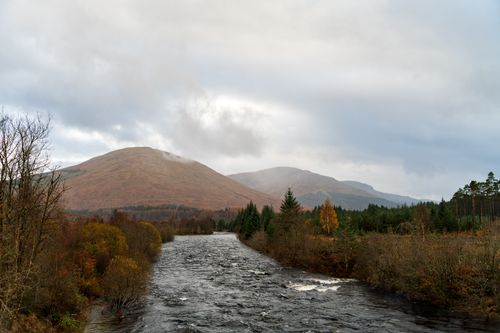 Free Serene landscape of a river flowing through autumn foliage with mountains in the background. Stock Photo