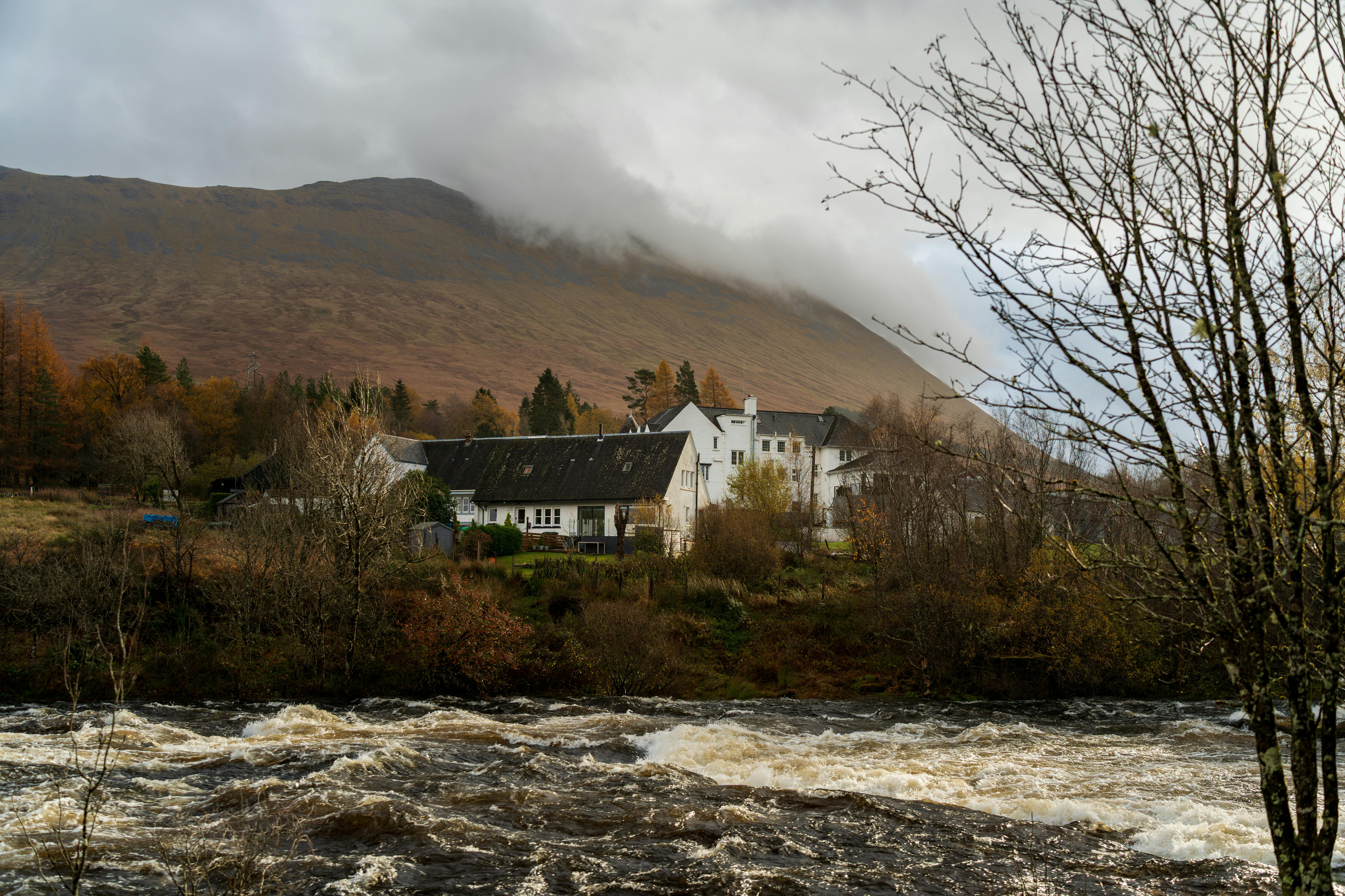 Picturesque view of a river flowing past rustic houses with a misty mountain backdrop.