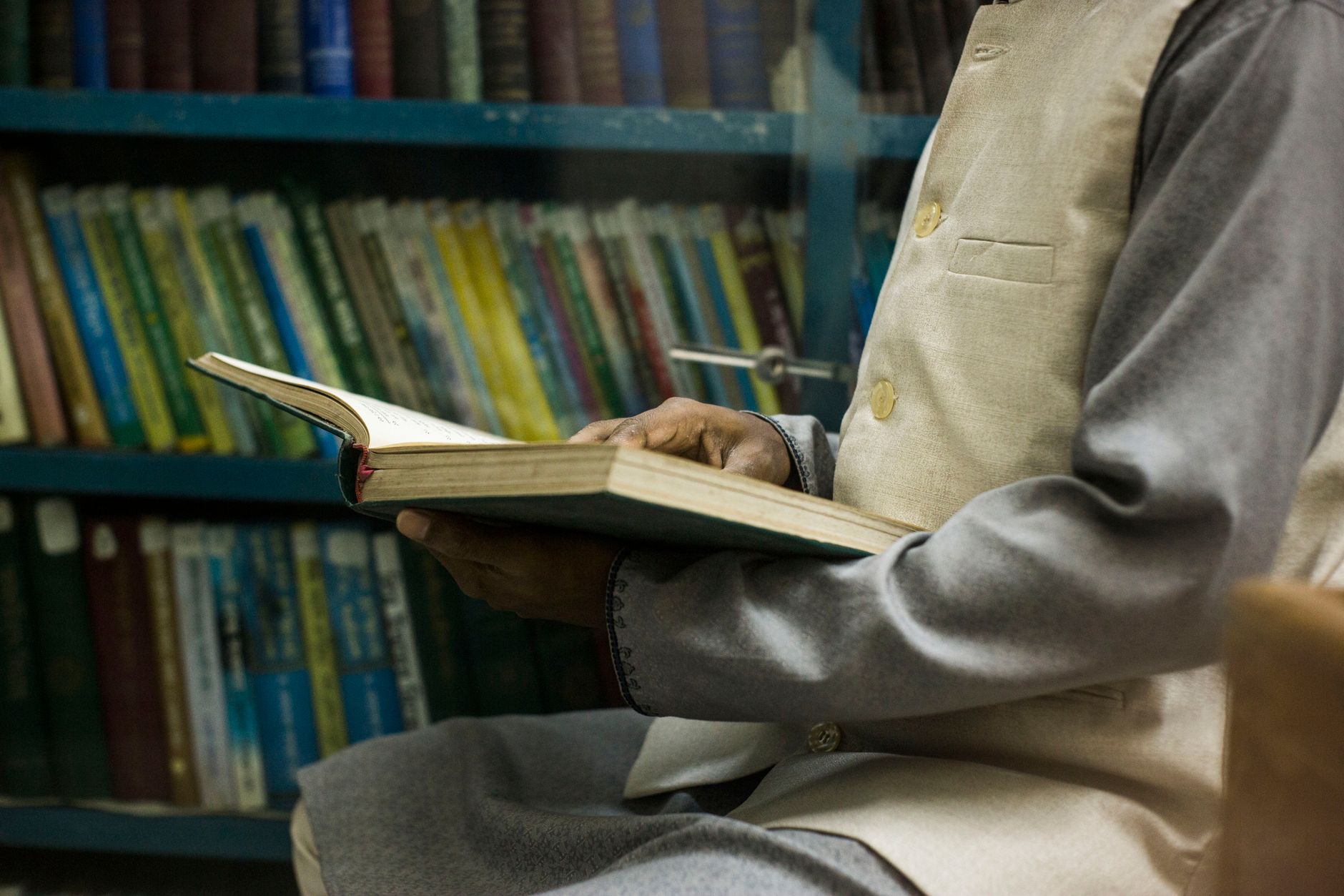 A person in traditional attire reading a book in a calm library environment, highlighting a focus on study and learning.