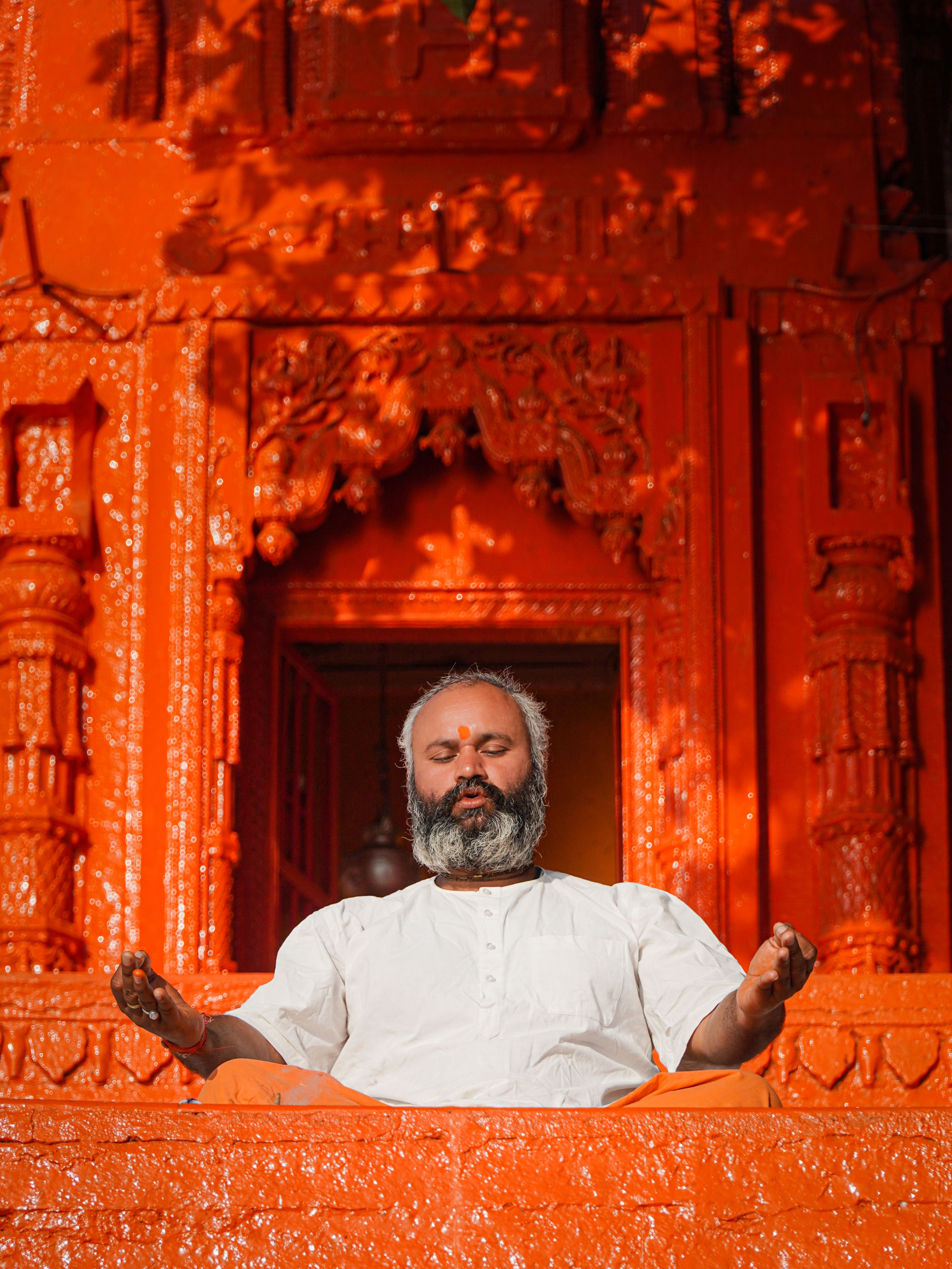 Peaceful meditation scene of a man in front of a vibrant orange temple in Varanasi, India.