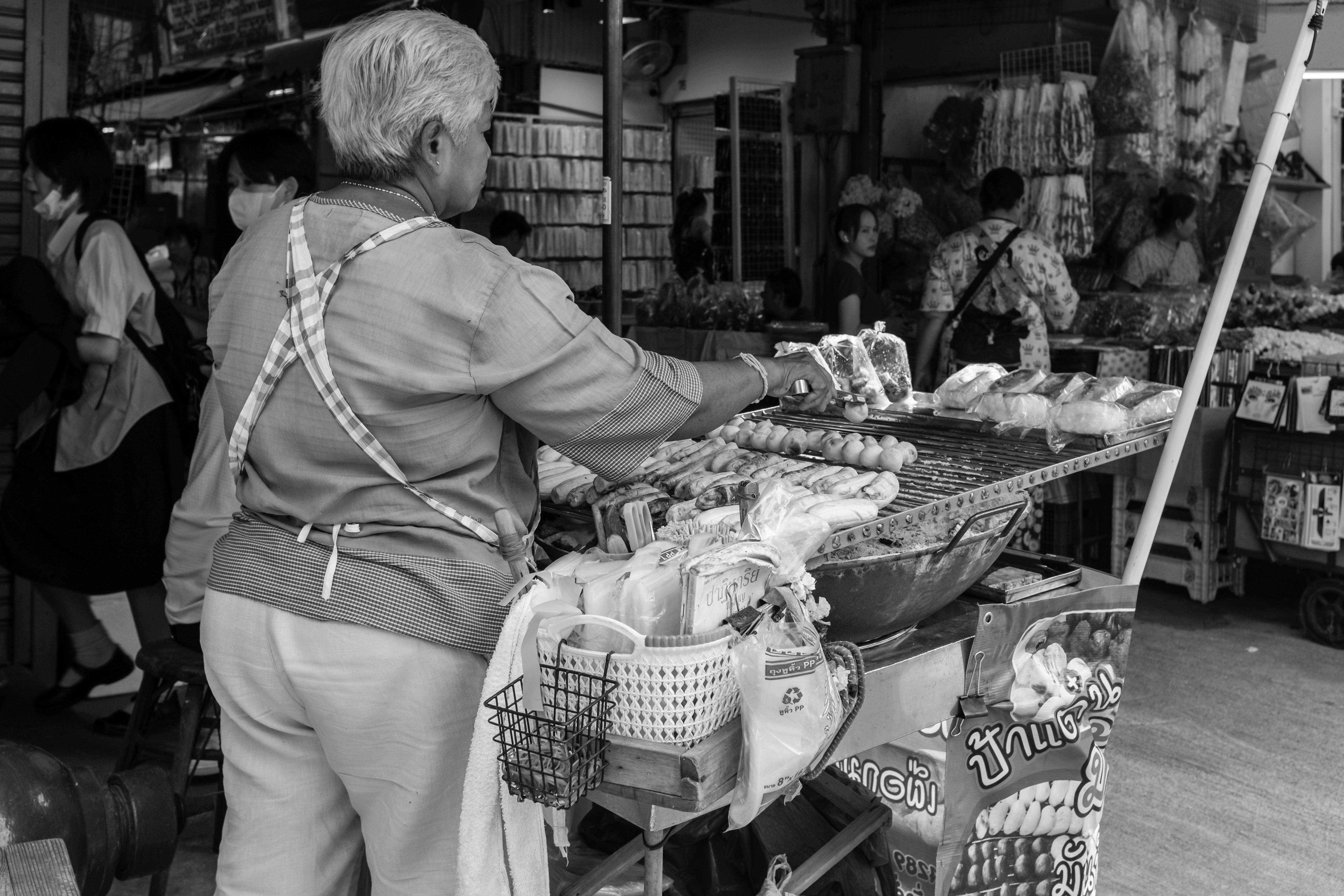 A street vendor grilling food in a bustling Asian market with various street foods on display.