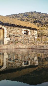 A picturesque stone house with a straw roof reflects in a thermal pool in Candarave, Tacna, Peru.