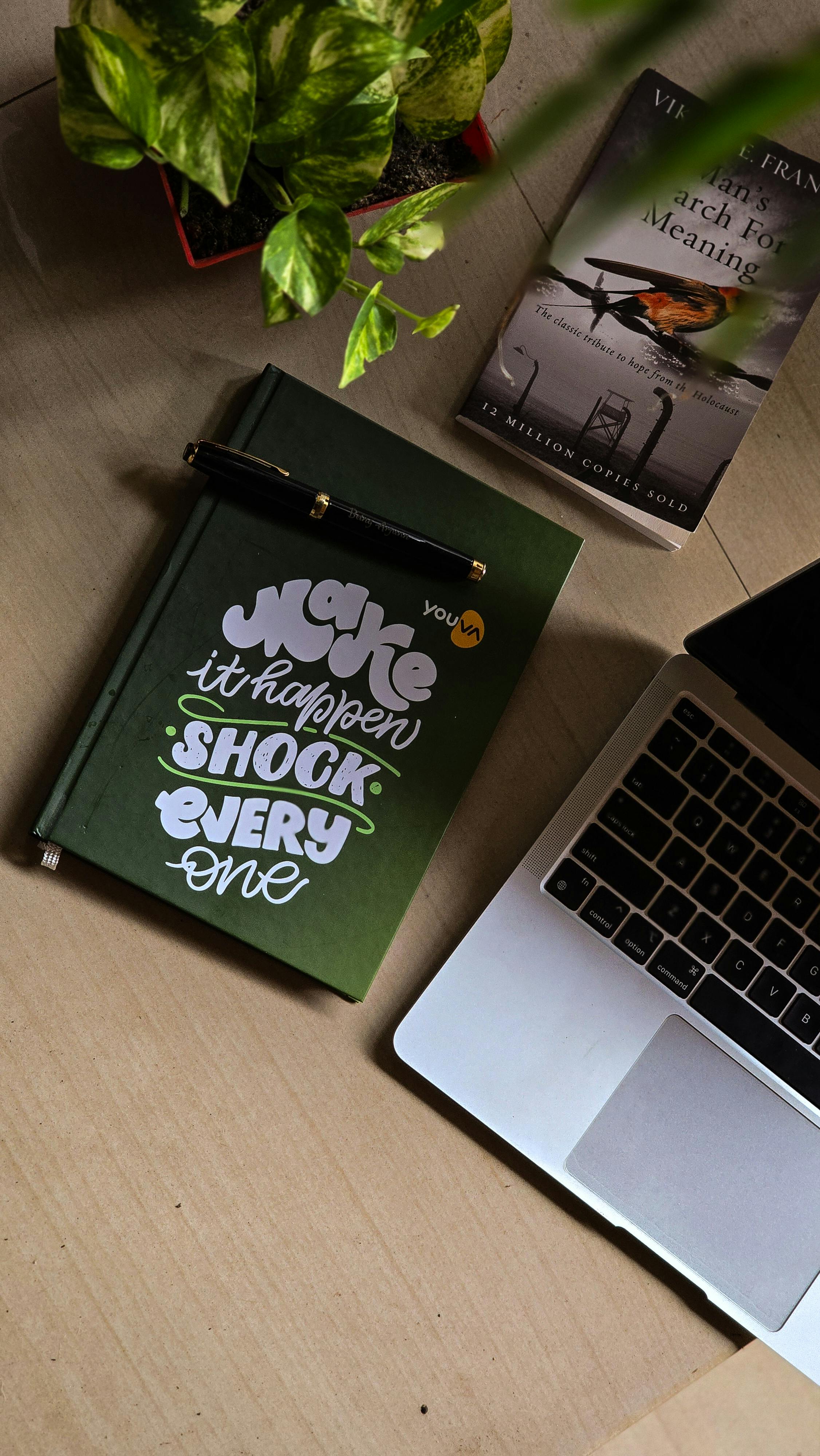 Kostenlos Ein stilvoller Arbeitsplatz mit Laptop, Motivationsjournal, Pflanze und Buch für eine inspirierende Arbeitsumgebung. Stock-Foto