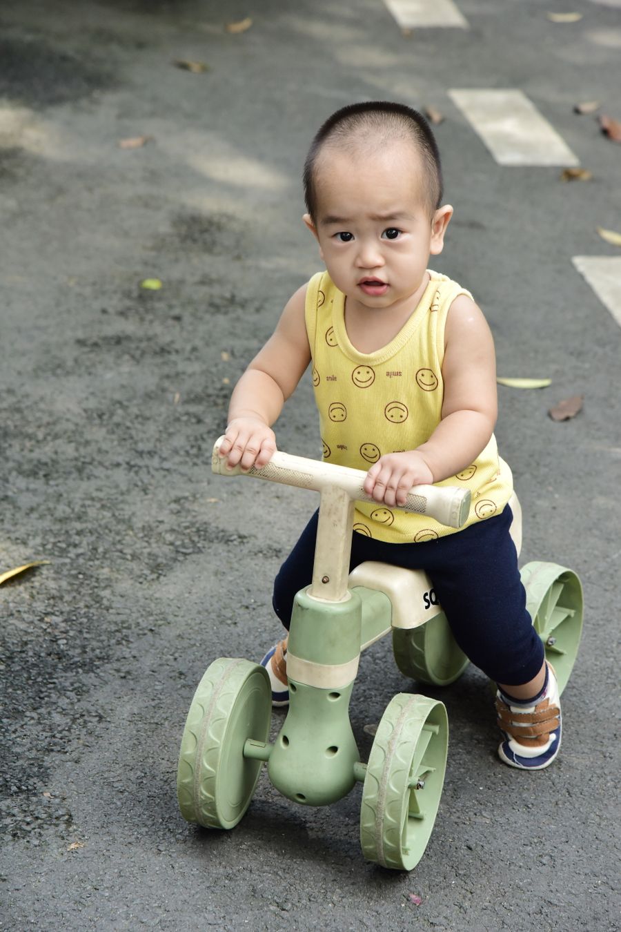 Toddler happily riding a green tricycle outdoors on a sunny day