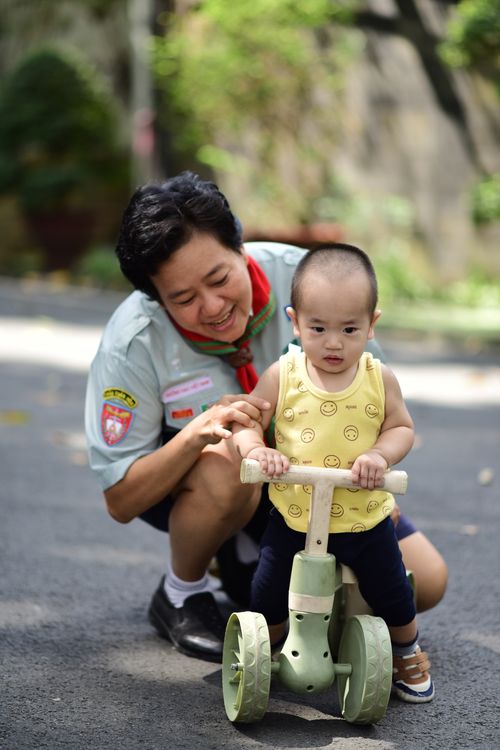 Child riding a tricycle with a caregiver outdoors