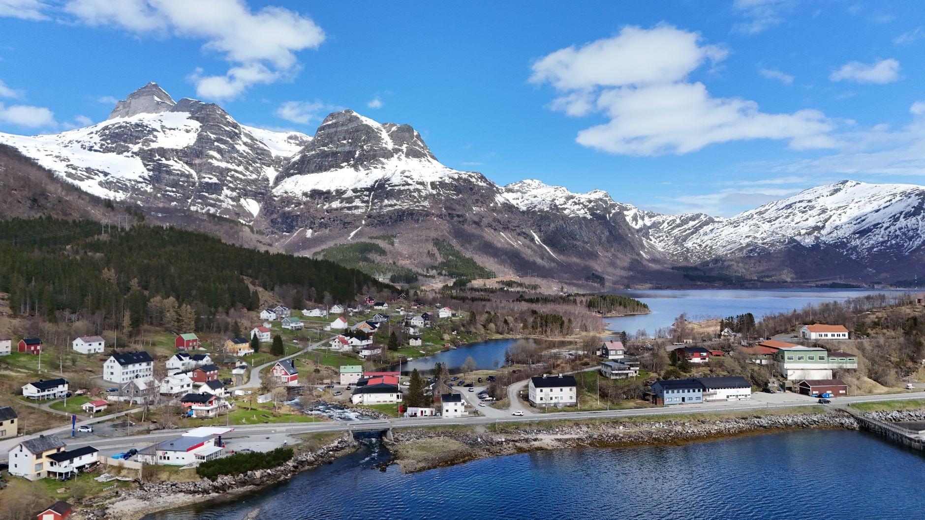 Aerial view of a Norwegian village with snow-capped mountains and a clear blue sky.