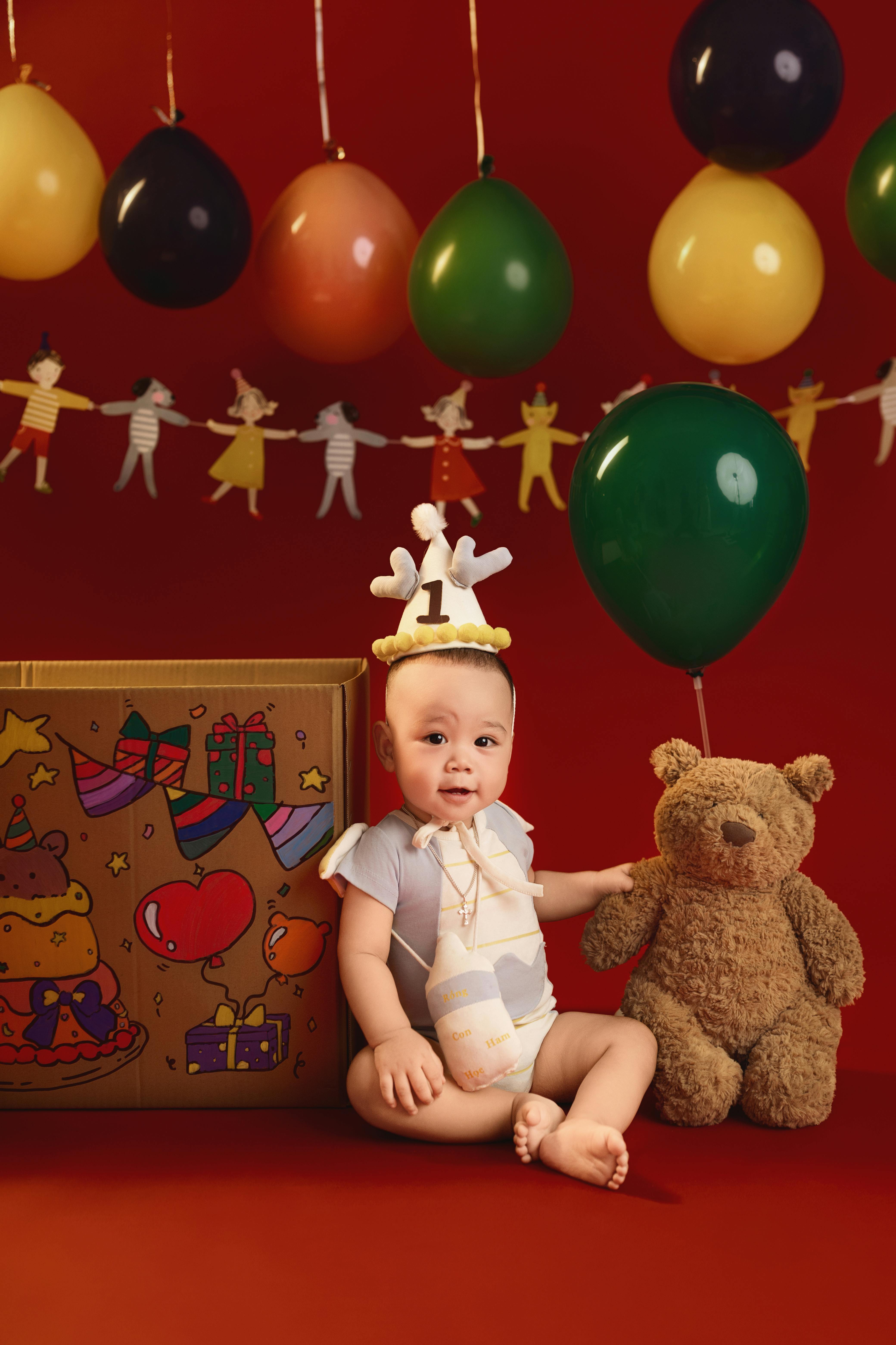 Cute baby celebrating first birthday with balloons and teddy bear in a festive setting.