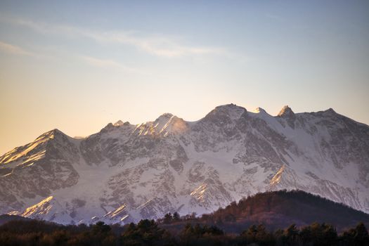 A stunning view of a snow-capped mountain range bathed in golden sunrise light, perfect for nature lovers.
