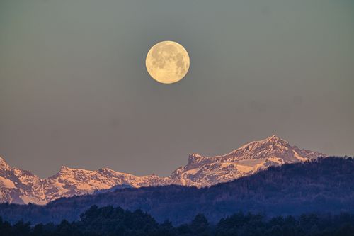 Free A breathtaking view of a full moon rising above snow-covered mountains during twilight. Stock Photo