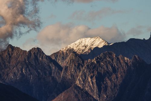 Free A stunning view of a snow-capped mountain peak surrounded by rugged terrain during sunset. Stock Photo