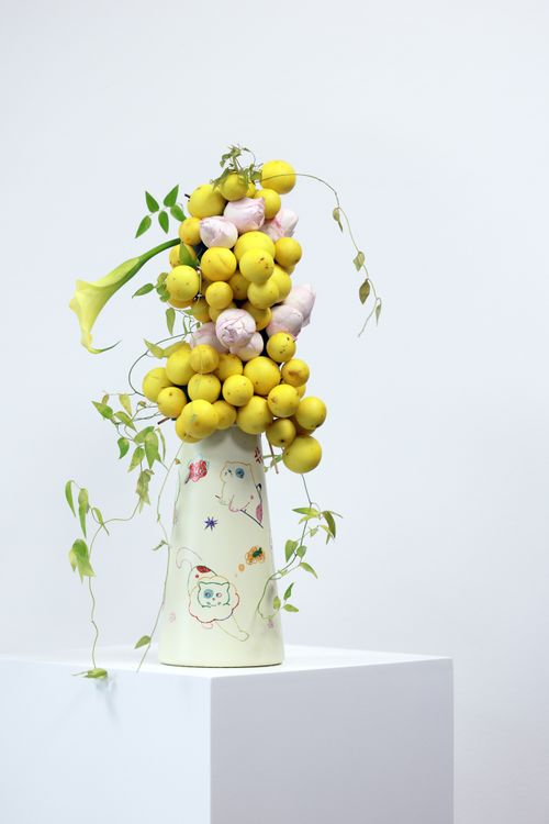 Free A creative still life of yellow fruits and greenery in a decorated vase against a white backdrop. Stock Photo