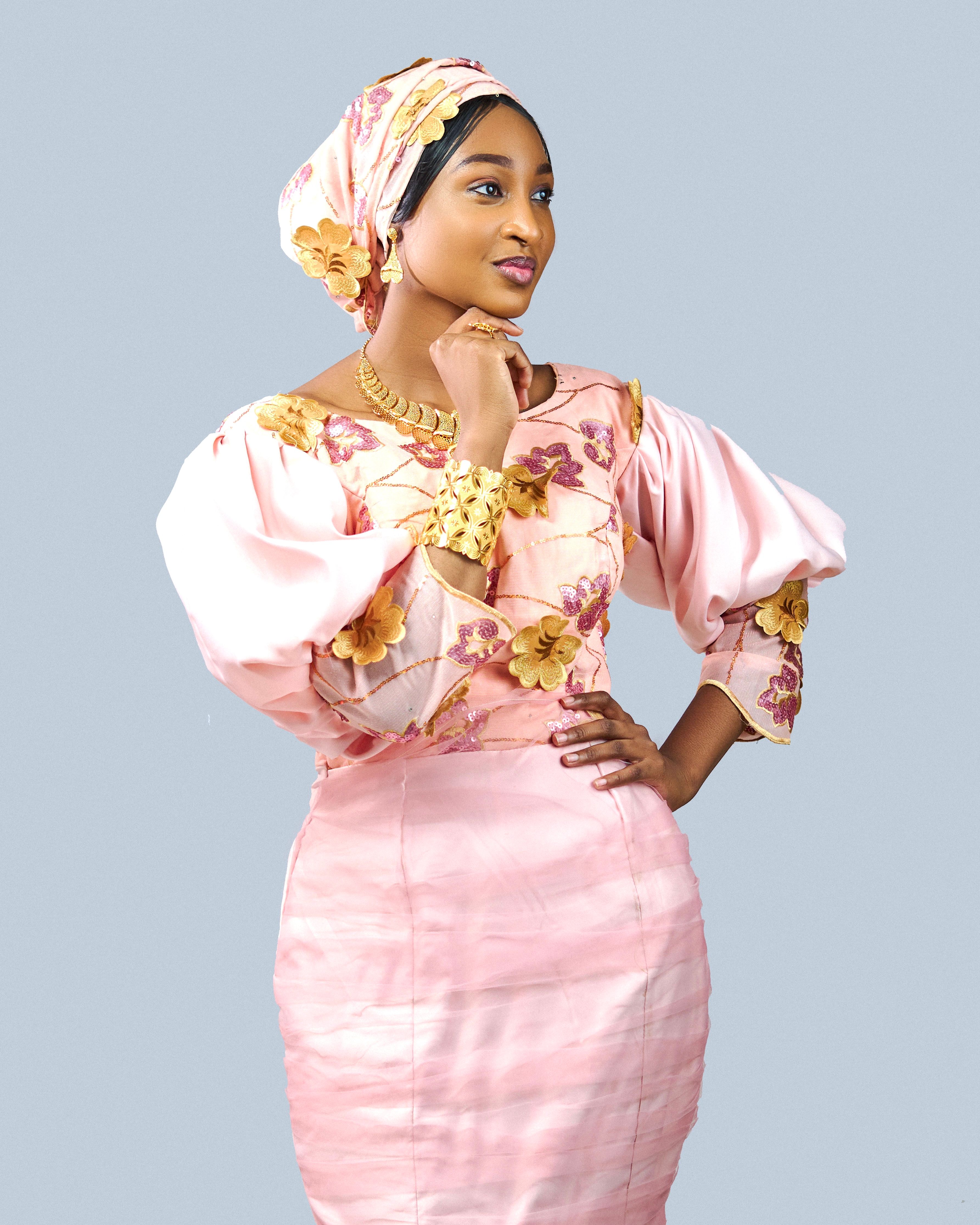 Stylish woman in pink traditional dress with floral designs poses thoughtfully.