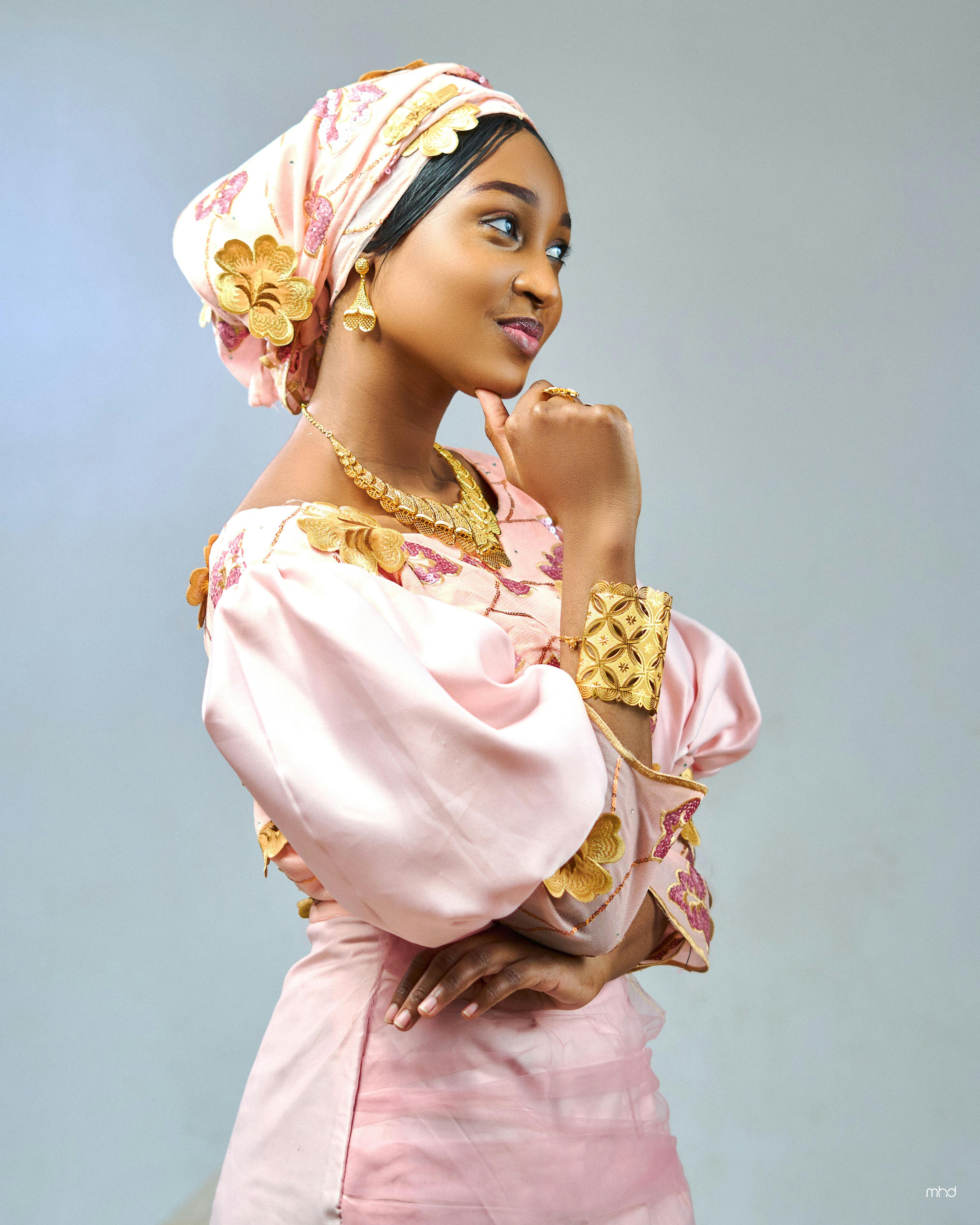 Elegant woman in pink traditional attire with floral headwrap and jewelry.