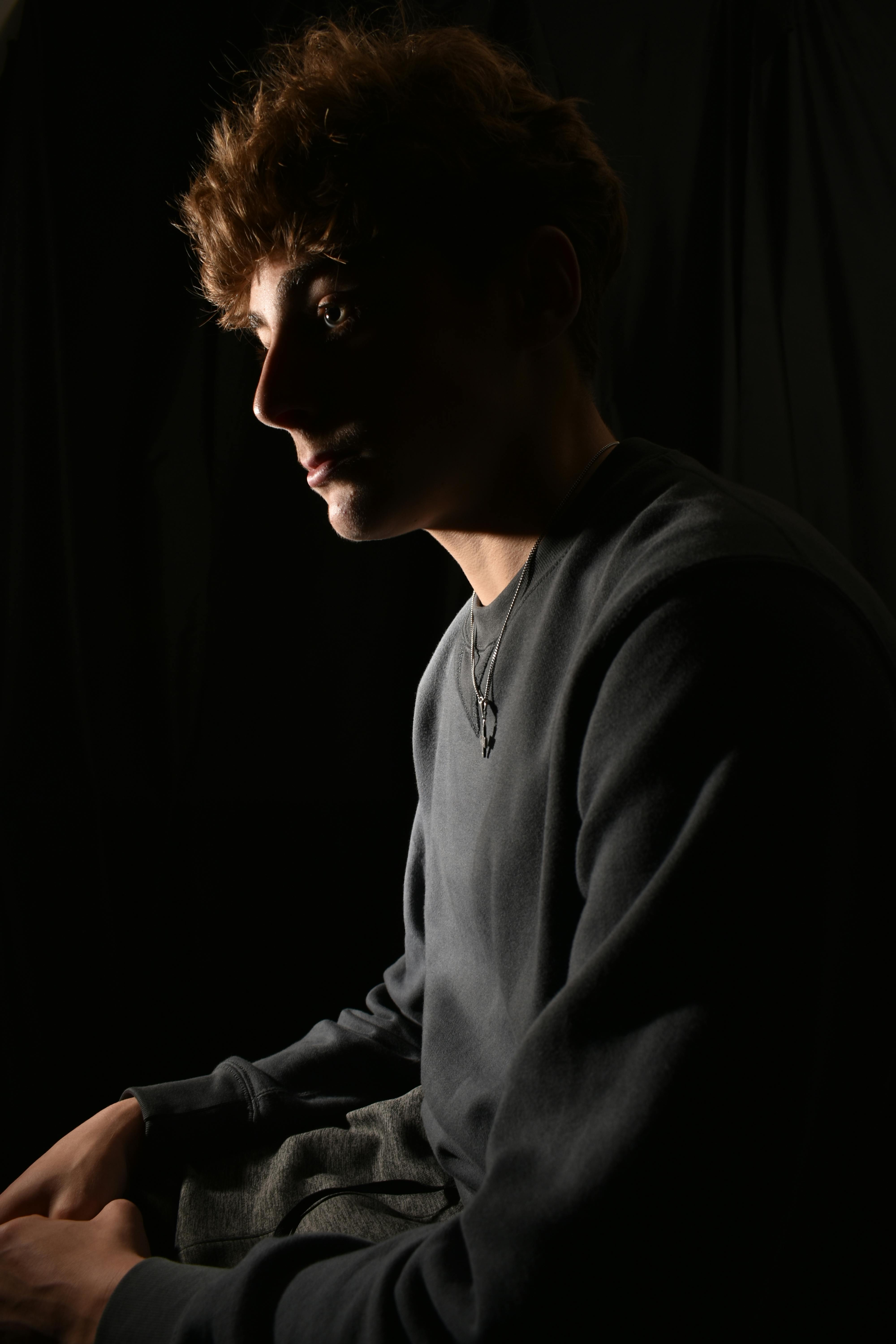 Dramatic side profile portrait of a young man in dim lighting, conveying mystery and depth.