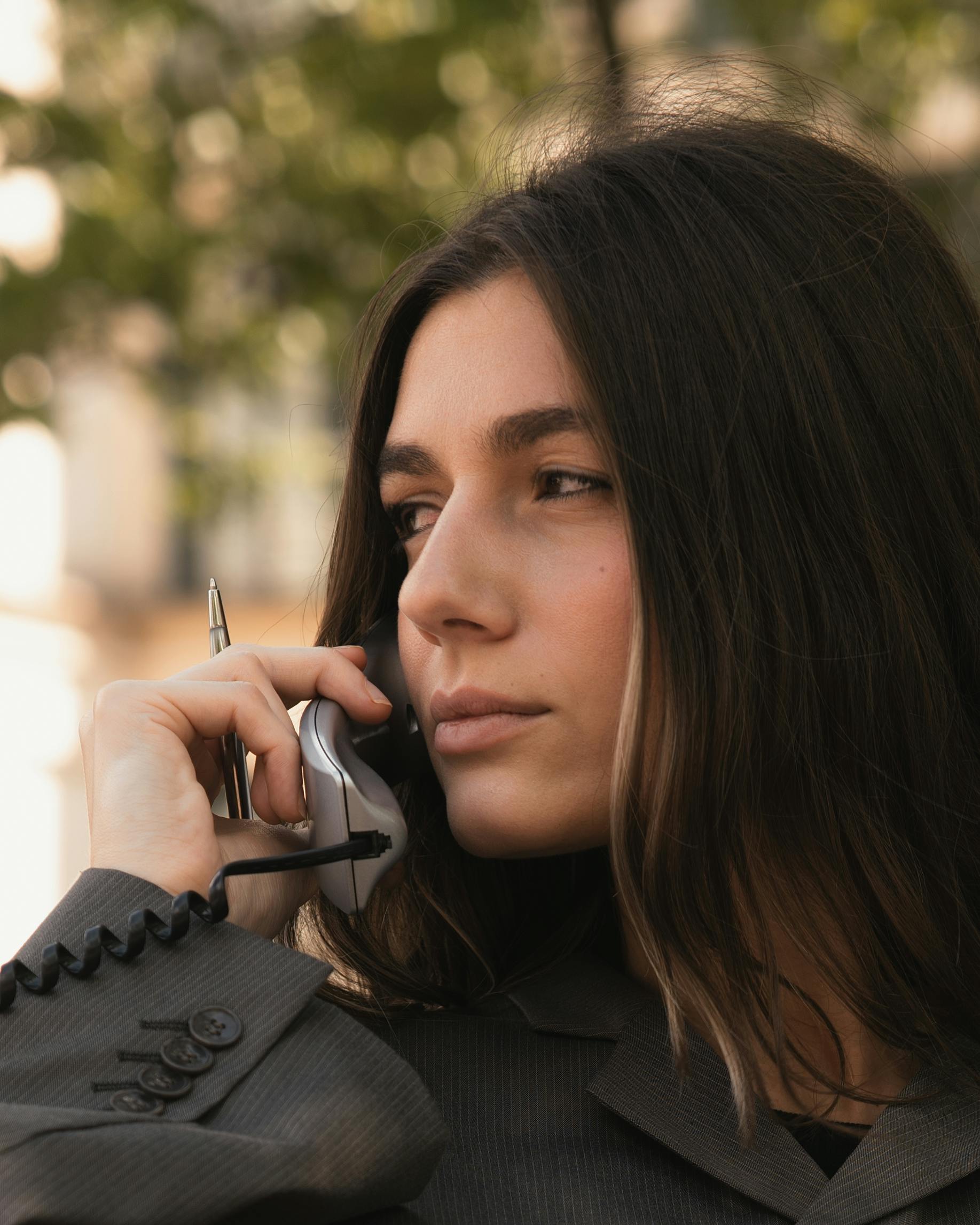 bezplatná Portrét mladé ženy v obchodním oblečení, která venku telefonuje se zamyšleným výrazem. Základová fotografie