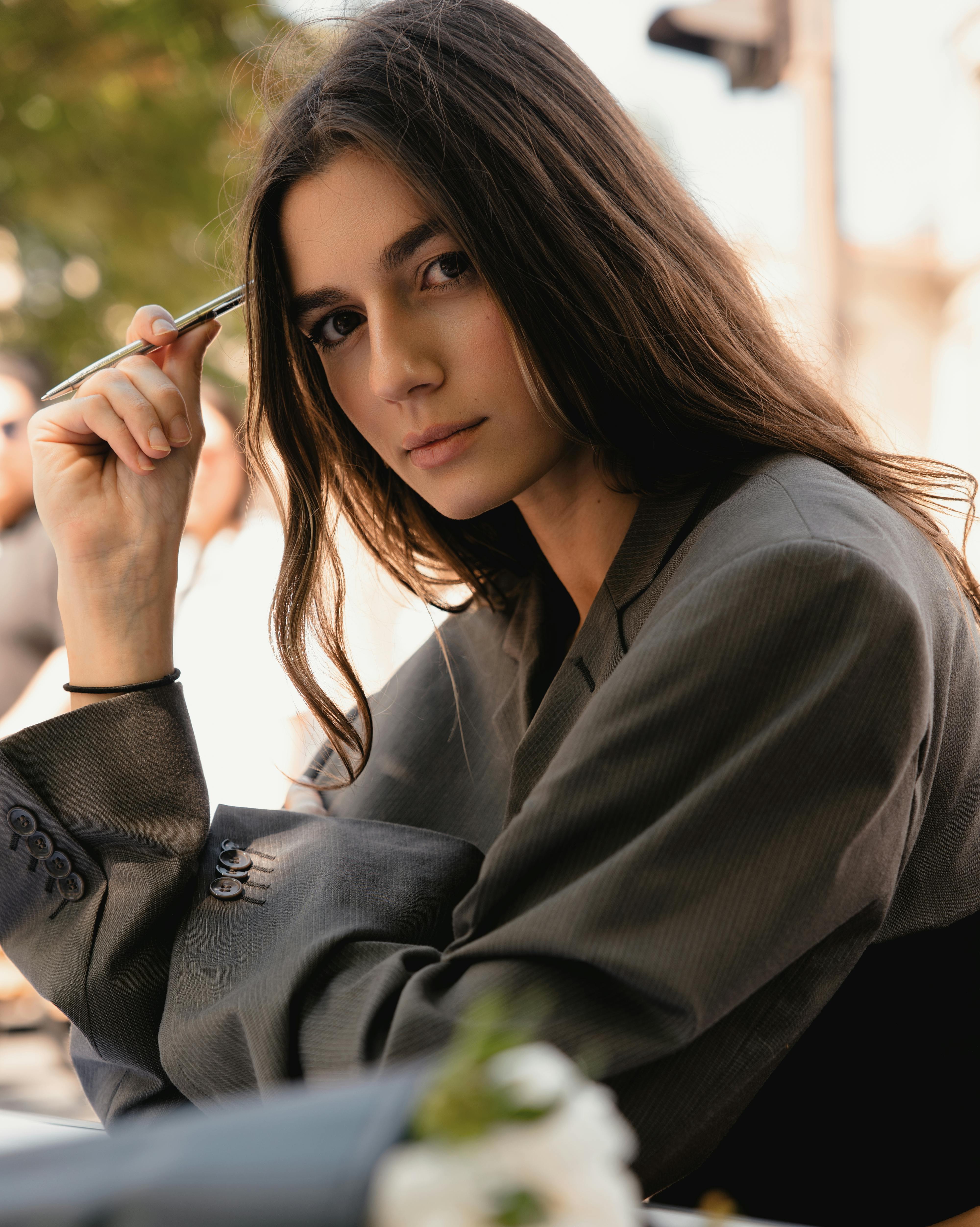 Confident young woman in business attire holding pen, outdoors setting.
