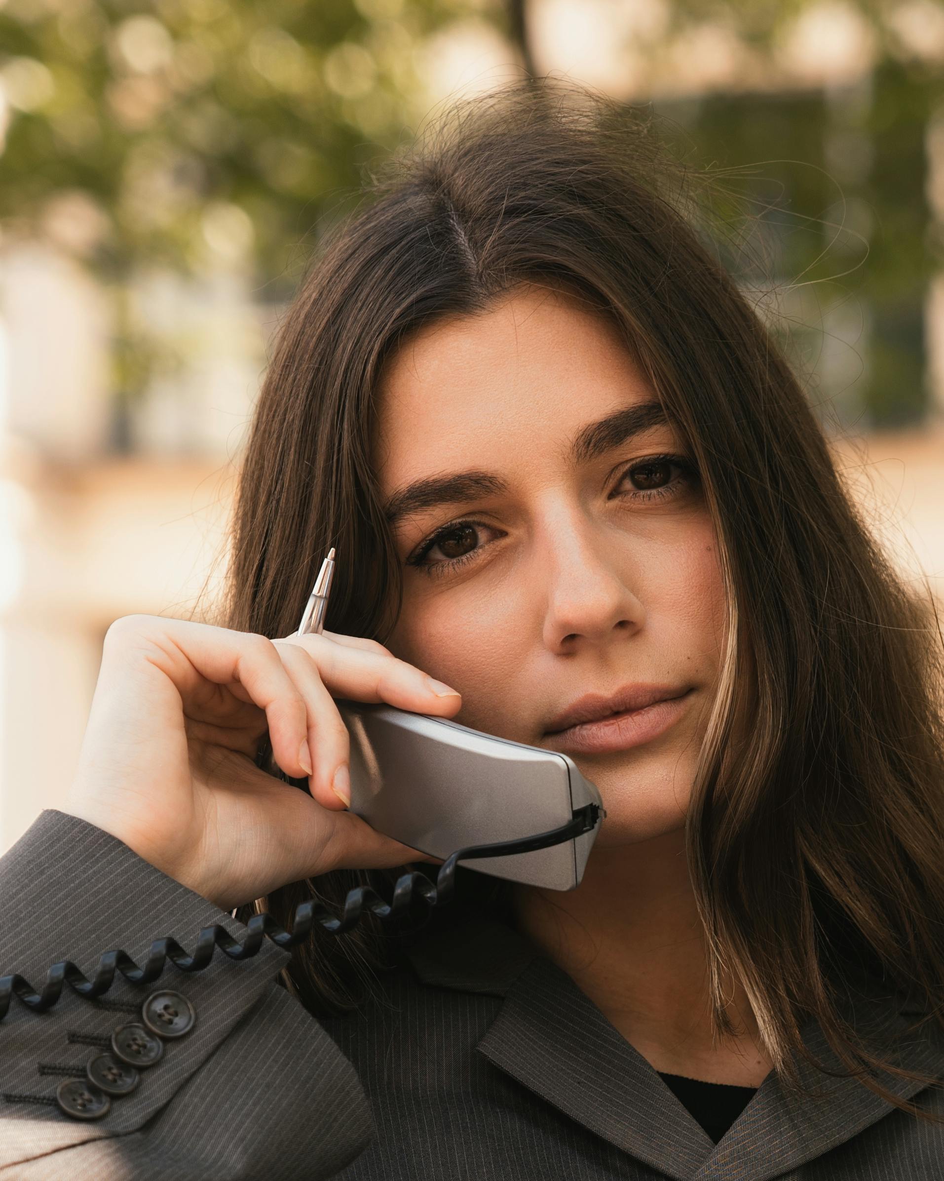 ฟรี นักธุรกิจสาวมั่นใจกำลังโทรออกผ่านโทรศัพท์แบบมีสายแบบดั้งเดิมกลางแจ้ง คลังภาพถ่าย