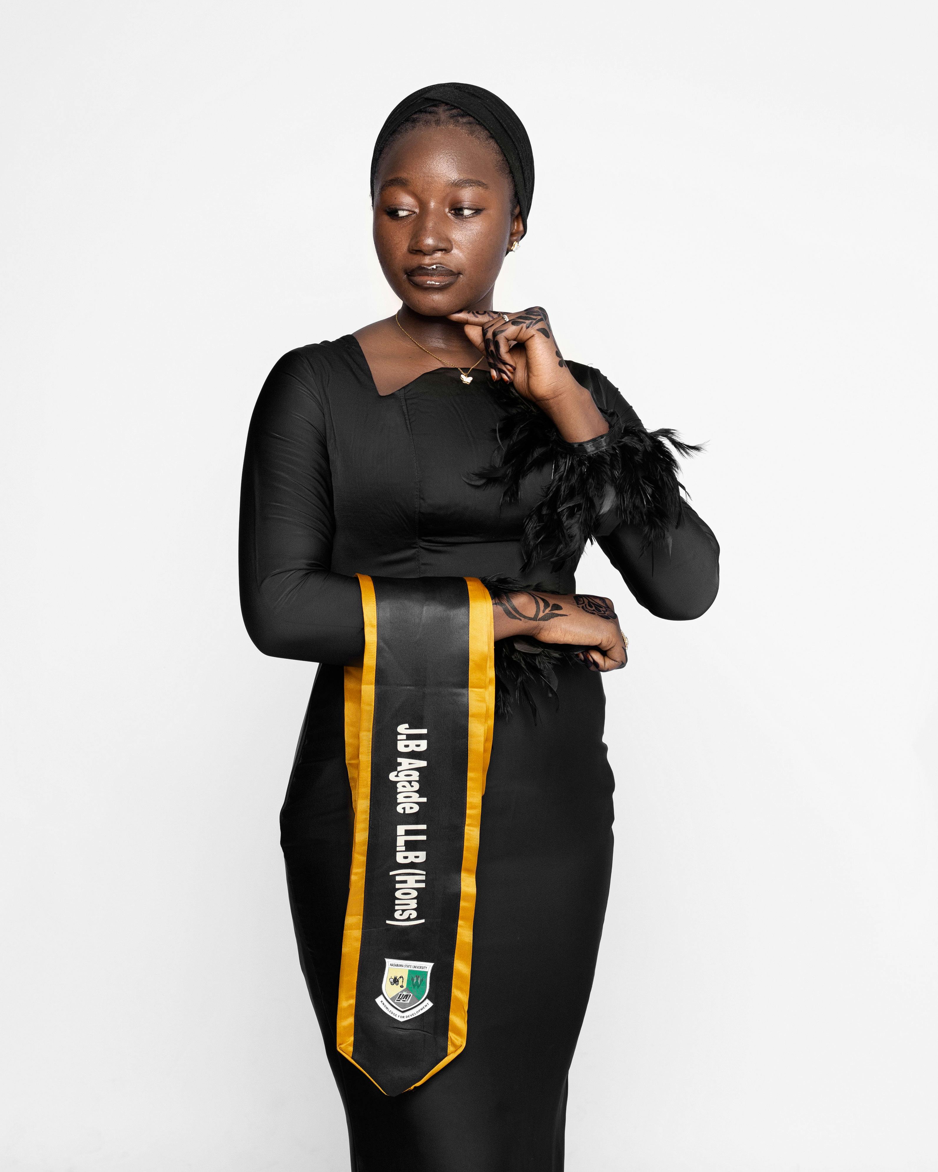Woman in black dress with academic sash poses for a formal graduation portrait.