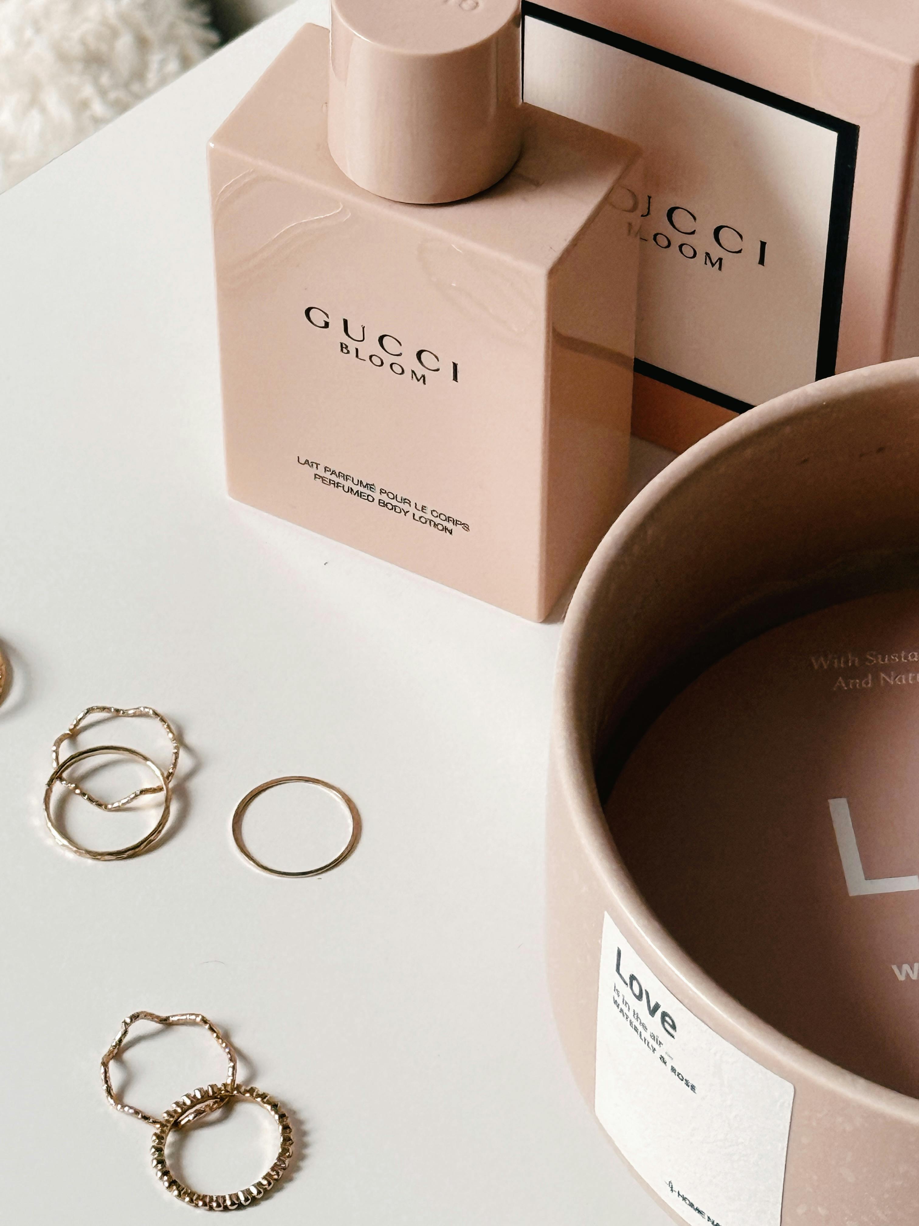 Elegantly styled Gucci Bloom perfume bottle with gold rings on a minimalist white background.