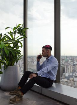 Man sits by window drinking coffee, overlooking cityscape from modern high-rise.