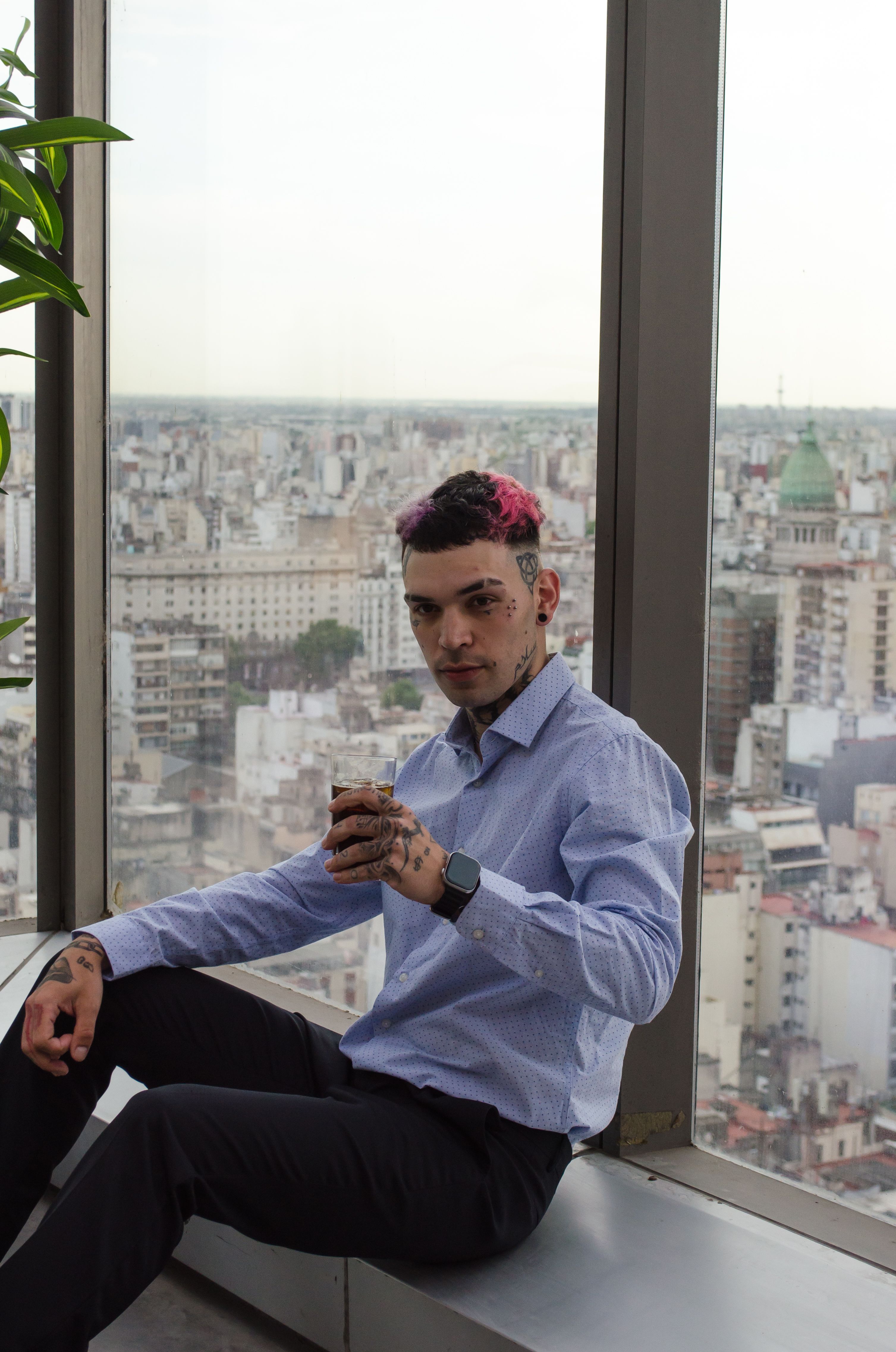 Businessman with tattoos enjoys a break in a modern high-rise lounge with city views.