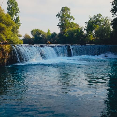 Free A tranquil waterfall cascading into a river surrounded by lush greenery, captured in natural daylight. Stock Photo