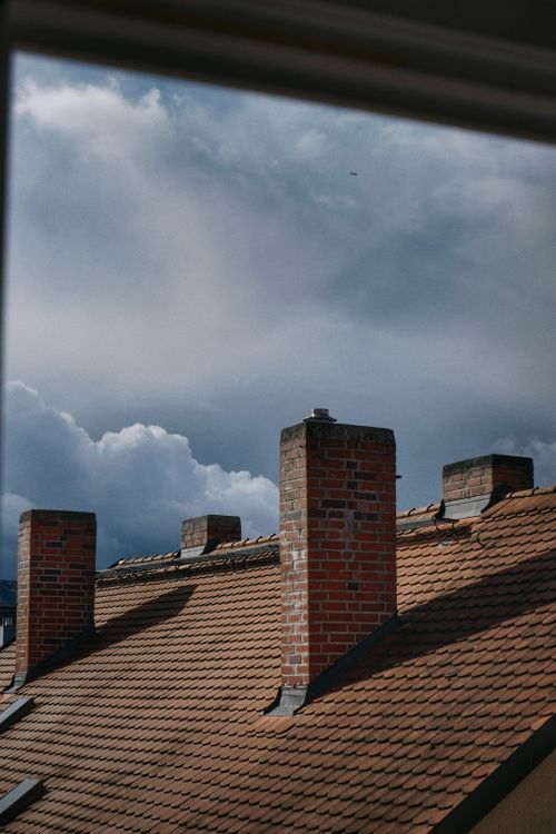 Free A dramatic view of brick chimneys on a tiled roof beneath a cloudy blue sky, capturing the essence of European architecture. Stock Photo