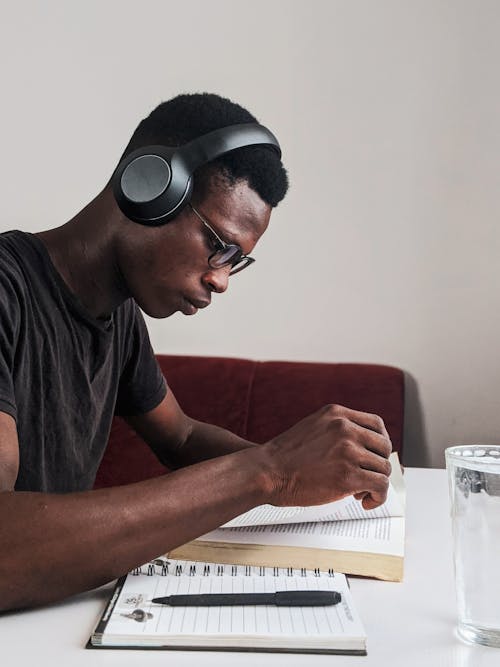 Hombre Vestido Con Camiseta Negra Con Cuello Redondo Con Auriculares Negros Leyendo Un Libro Mientras Está Sentado