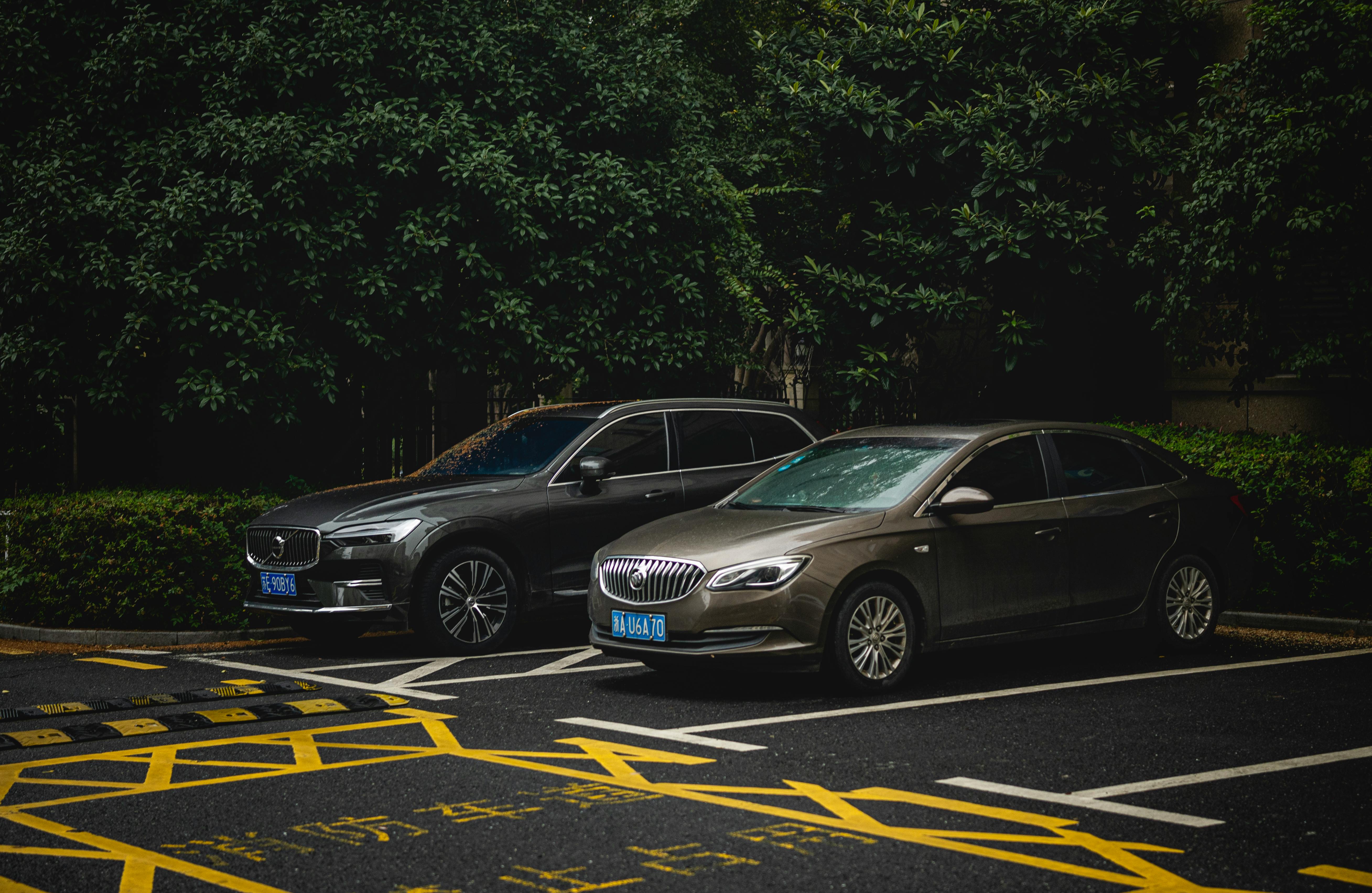 Two cars, an SUV and a sedan, parked side by side in a shady urban lot.