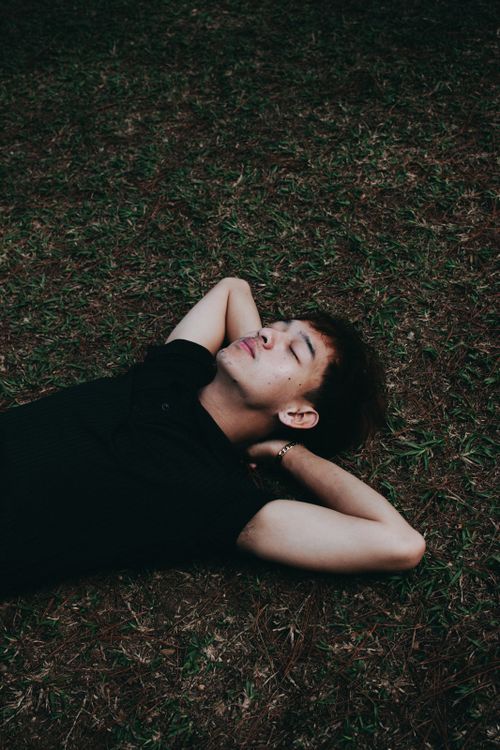 Free A young man in a black shirt relaxes outdoors on the grassy ground. Stock Photo